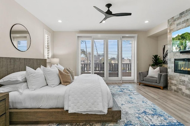 bedroom featuring ceiling fan, hardwood / wood-style floors, access to outside, and a fireplace