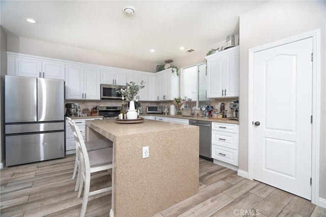 kitchen featuring a breakfast bar, tasteful backsplash, white cabinets, a center island, and stainless steel appliances