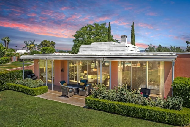 back house at dusk featuring a yard and a patio