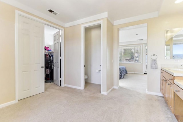 unfurnished bedroom featuring light carpet, a closet, sink, and ensuite bath