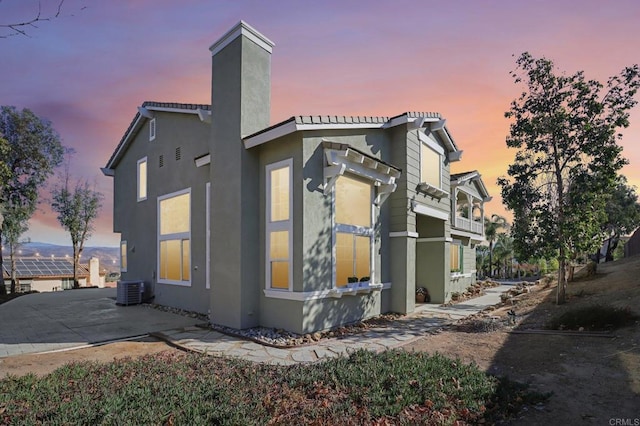 property exterior at dusk featuring central air condition unit and a patio