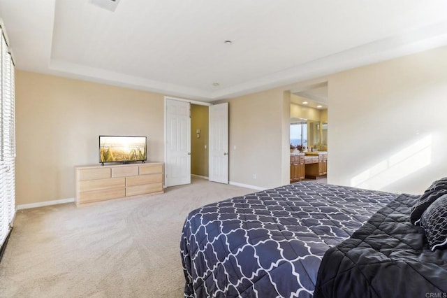 carpeted bedroom featuring ensuite bathroom and a tray ceiling