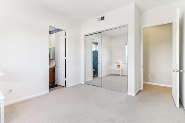 unfurnished bedroom with ensuite bath, light colored carpet, and a closet