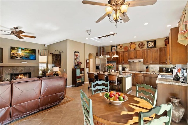 dining room with ceiling fan, a tile fireplace, and light tile patterned floors