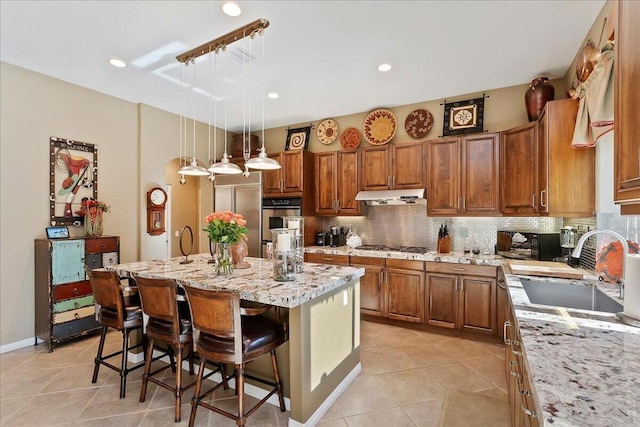 kitchen featuring pendant lighting, sink, a breakfast bar, light stone countertops, and a center island with sink