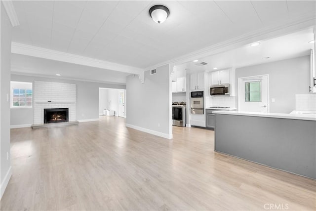 unfurnished living room with a brick fireplace, crown molding, and light hardwood / wood-style floors