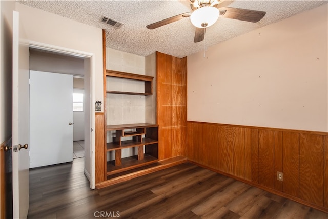 interior space with ceiling fan, dark hardwood / wood-style flooring, wooden walls, and a textured ceiling