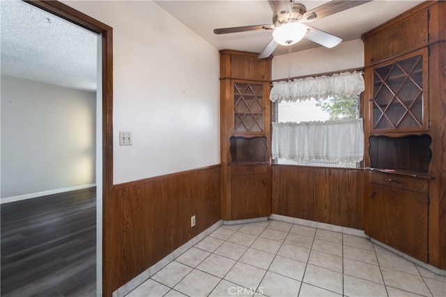 unfurnished dining area with ceiling fan, wood walls, and a textured ceiling