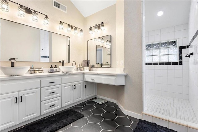 bathroom with tile patterned flooring, vanity, vaulted ceiling, and tiled shower