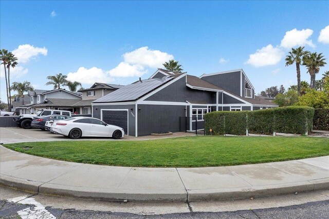 view of front of home featuring a garage, a front lawn, and solar panels