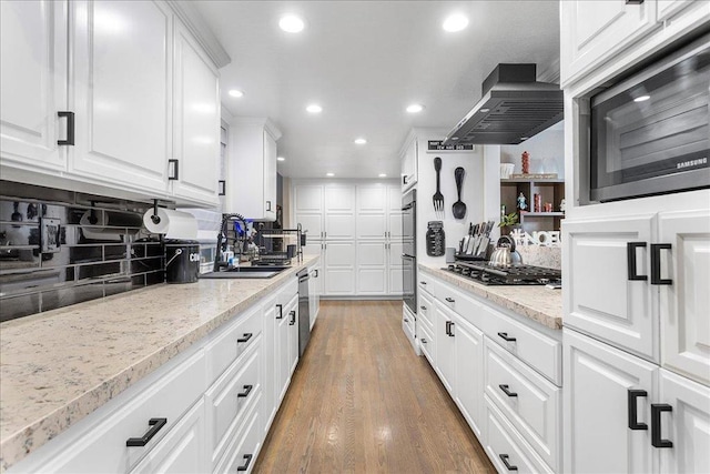 kitchen featuring appliances with stainless steel finishes, white cabinets, backsplash, island exhaust hood, and light stone countertops