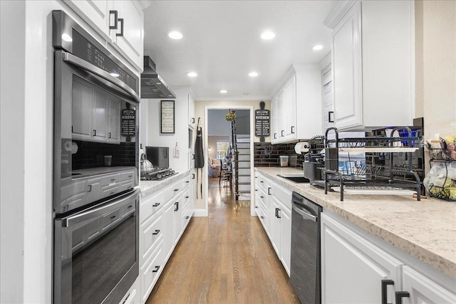 kitchen with white cabinetry, stainless steel appliances, wall chimney exhaust hood, and light stone counters