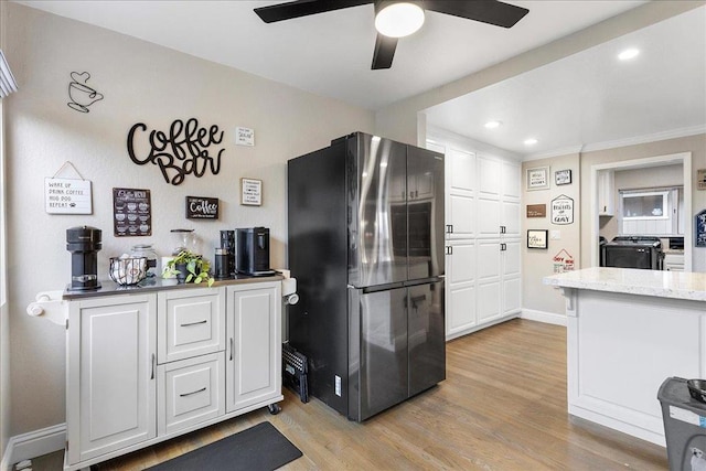 kitchen with refrigerator, white cabinets, ceiling fan, light stone counters, and light hardwood / wood-style floors