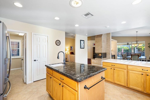 kitchen with a center island with sink, stainless steel fridge, light tile patterned flooring, a fireplace, and sink