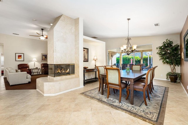 dining space featuring ceiling fan with notable chandelier, a multi sided fireplace, and vaulted ceiling