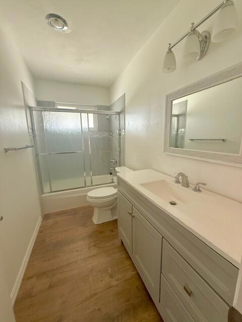 full bathroom with toilet, vanity, combined bath / shower with glass door, and hardwood / wood-style flooring