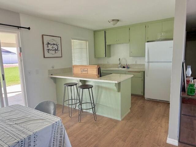 kitchen with white fridge, a kitchen breakfast bar, sink, kitchen peninsula, and green cabinetry