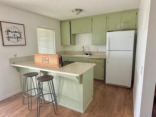 kitchen featuring white fridge, green cabinetry, kitchen peninsula, and sink