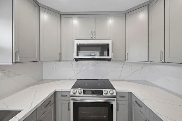 kitchen featuring appliances with stainless steel finishes, decorative backsplash, light stone counters, and gray cabinets