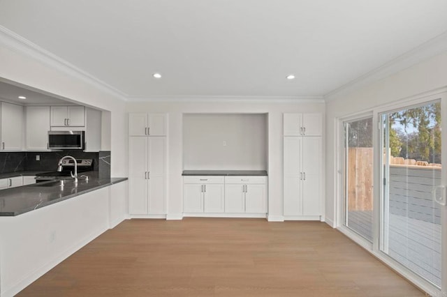 kitchen with stainless steel appliances, crown molding, light hardwood / wood-style flooring, and backsplash