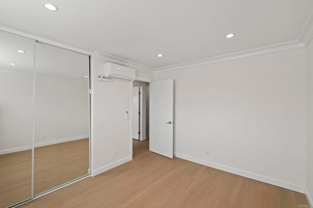 unfurnished bedroom with a closet, light hardwood / wood-style flooring, crown molding, and a wall mounted AC