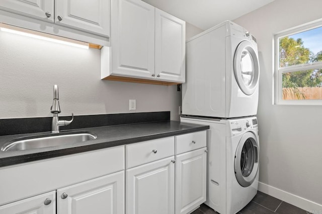 laundry room with stacked washer and dryer, dark tile patterned flooring, sink, and cabinets