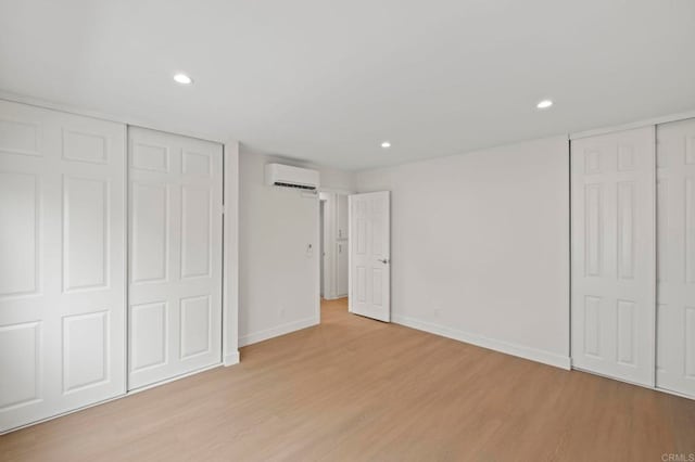 unfurnished bedroom with light wood-type flooring, multiple closets, and a wall mounted air conditioner