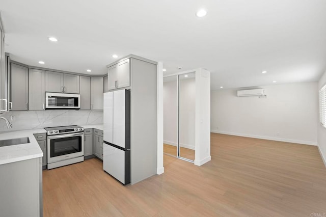 kitchen featuring electric stove, a wall mounted AC, gray cabinets, white fridge, and light hardwood / wood-style floors