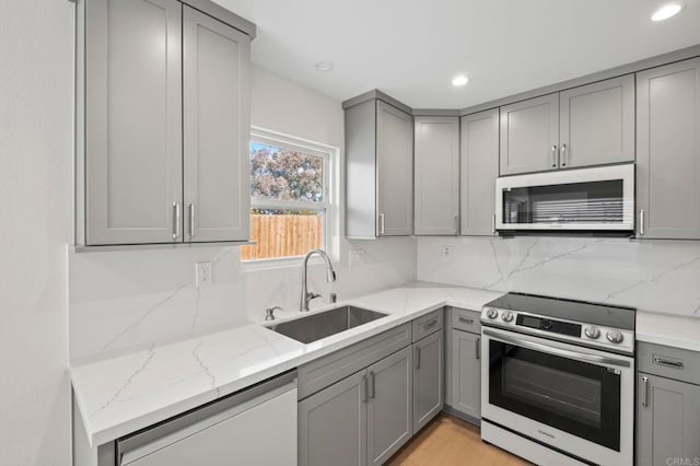 kitchen with light stone countertops, gray cabinets, stainless steel appliances, and sink