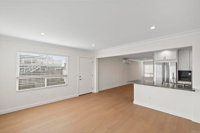 unfurnished living room featuring a wealth of natural light, ornamental molding, light hardwood / wood-style flooring, and sink