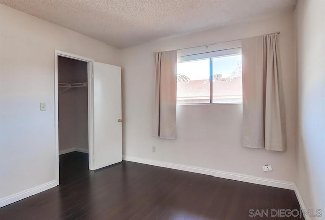 unfurnished bedroom featuring a spacious closet, dark wood-type flooring, a textured ceiling, and a closet