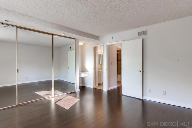 unfurnished bedroom with dark wood-type flooring, a textured ceiling, ensuite bathroom, and a closet