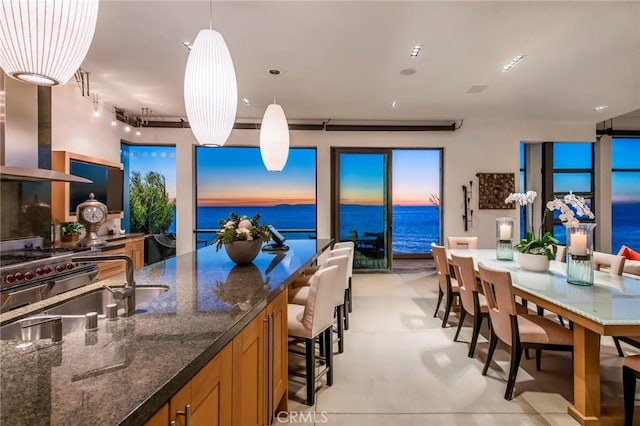 kitchen featuring pendant lighting, sink, dark stone countertops, a water view, and wall chimney exhaust hood