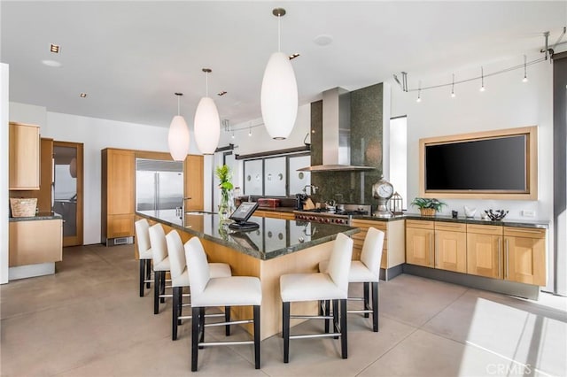 kitchen featuring a breakfast bar, dark stone counters, hanging light fixtures, stainless steel appliances, and wall chimney exhaust hood