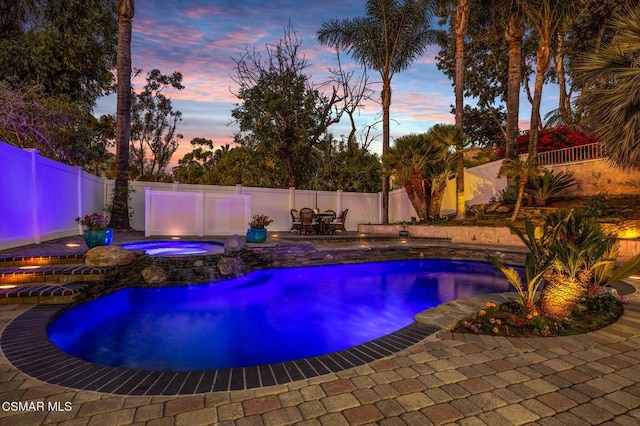 pool at dusk featuring a patio and an in ground hot tub