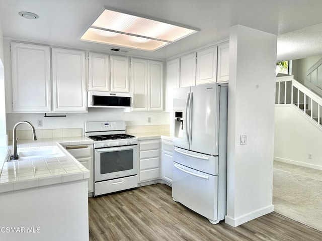 kitchen featuring tile countertops, kitchen peninsula, white appliances, white cabinets, and sink