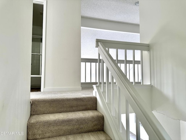 stairway featuring a textured ceiling and carpet floors