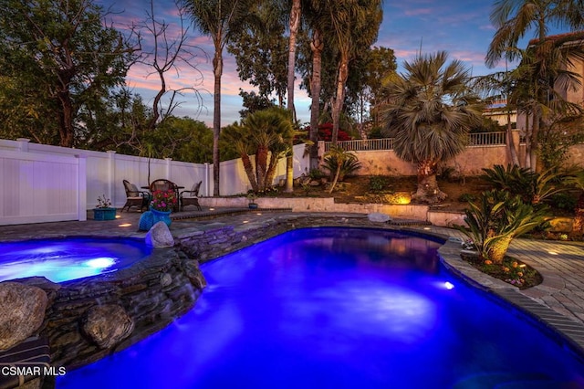 pool at dusk with an in ground hot tub and a patio