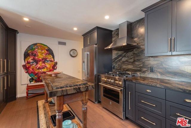 kitchen with appliances with stainless steel finishes, wall chimney exhaust hood, decorative backsplash, and light hardwood / wood-style floors