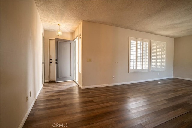 empty room featuring dark wood-type flooring, a textured ceiling, and a notable chandelier