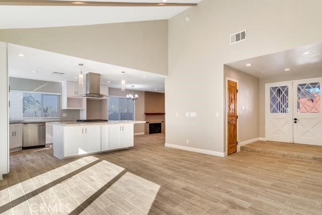 kitchen featuring pendant lighting, white cabinets, a center island, island range hood, and stainless steel dishwasher