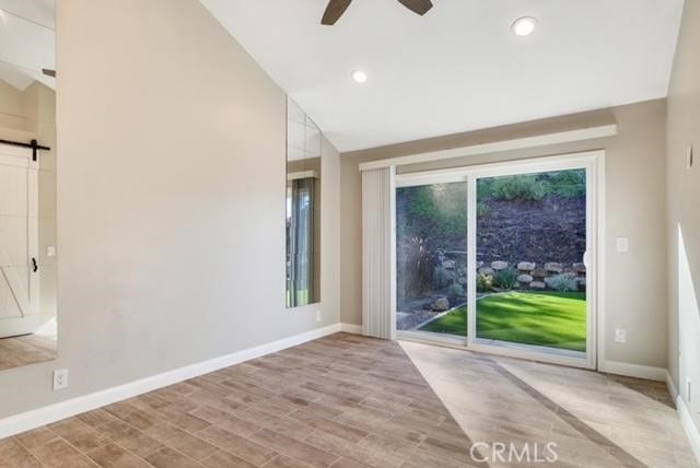 spare room featuring ceiling fan, light hardwood / wood-style flooring, a barn door, and vaulted ceiling