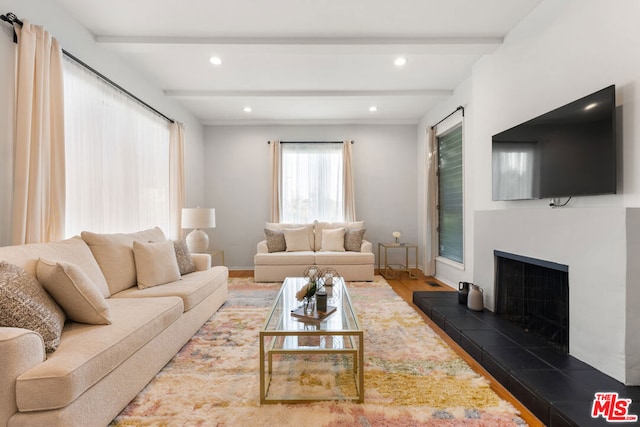 living room featuring dark wood-type flooring, a tile fireplace, and beamed ceiling