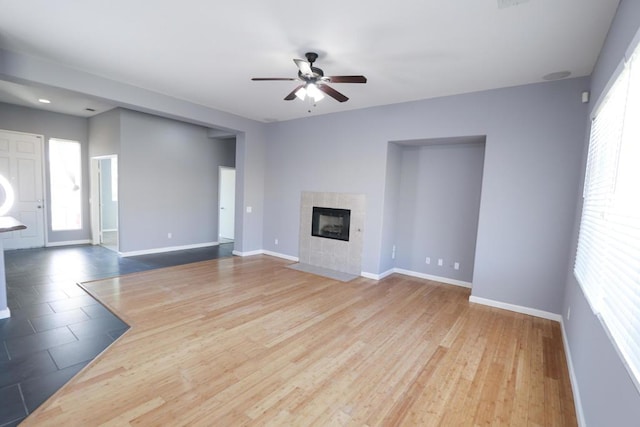 unfurnished living room featuring a tiled fireplace, wood-type flooring, and ceiling fan