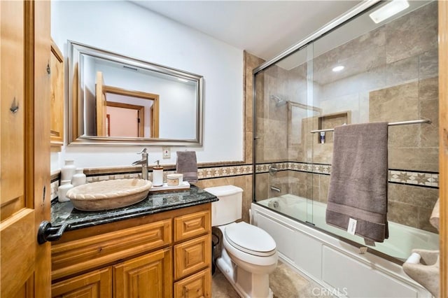 full bathroom featuring toilet, enclosed tub / shower combo, tile walls, and vanity