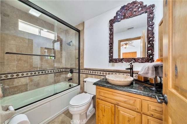 full bathroom featuring toilet, vanity, tile walls, tile patterned floors, and combined bath / shower with glass door