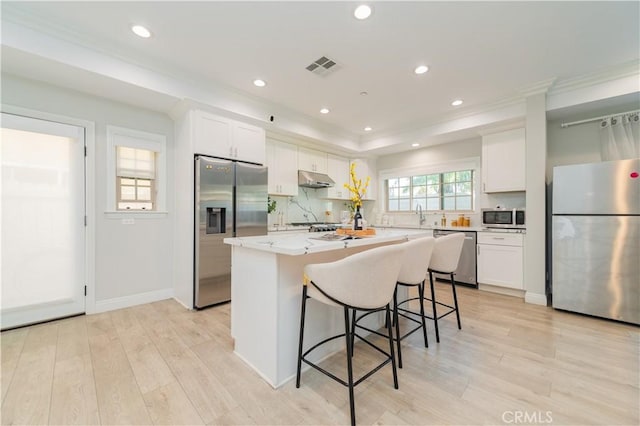 kitchen with visible vents, a kitchen island, appliances with stainless steel finishes, under cabinet range hood, and white cabinetry