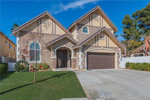 tudor home with driveway, a front lawn, fence, and stucco siding