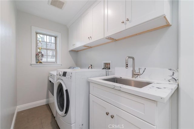 clothes washing area with separate washer and dryer, a sink, visible vents, baseboards, and cabinet space