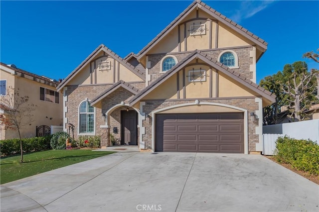 tudor-style house featuring stucco siding, concrete driveway, fence, a garage, and a front lawn